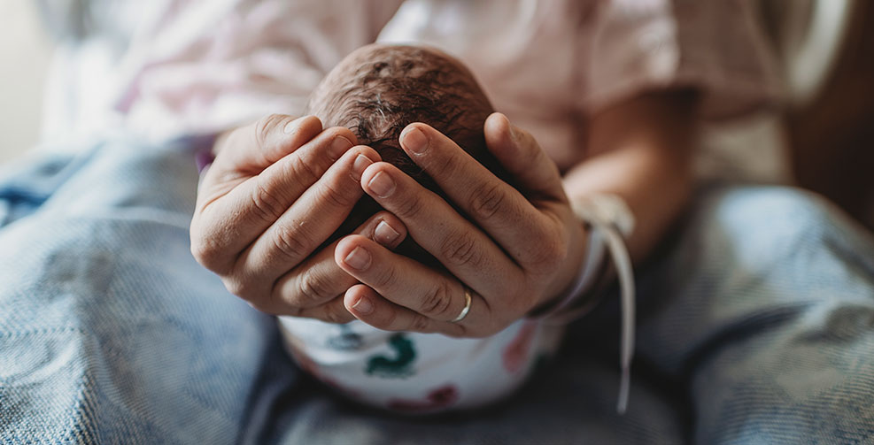 Close up image of the tops of a newborn's head resting in their mother's two hands