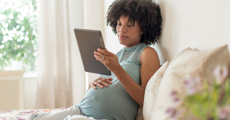 Pregnant woman sitting on her couch looking at her tablet