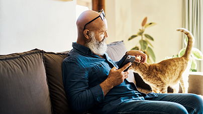 Older man petting his cat while looking on his phone