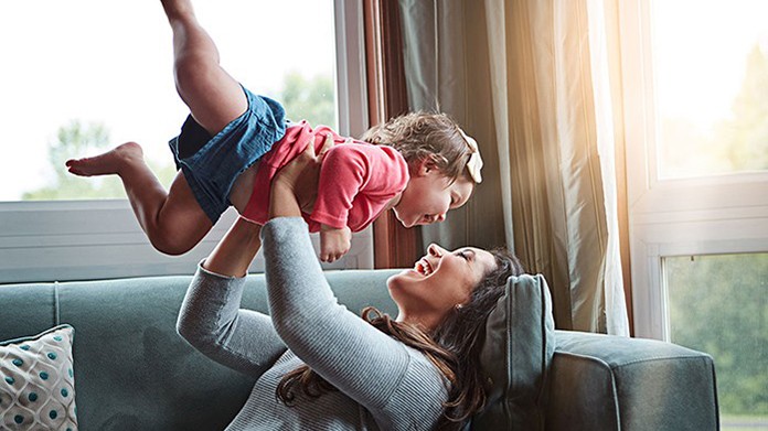 mom holding up toddler daughter on the couch